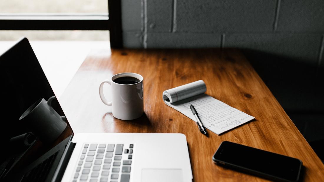 close-up of a laptop, coffee, and notepad on a wooden table