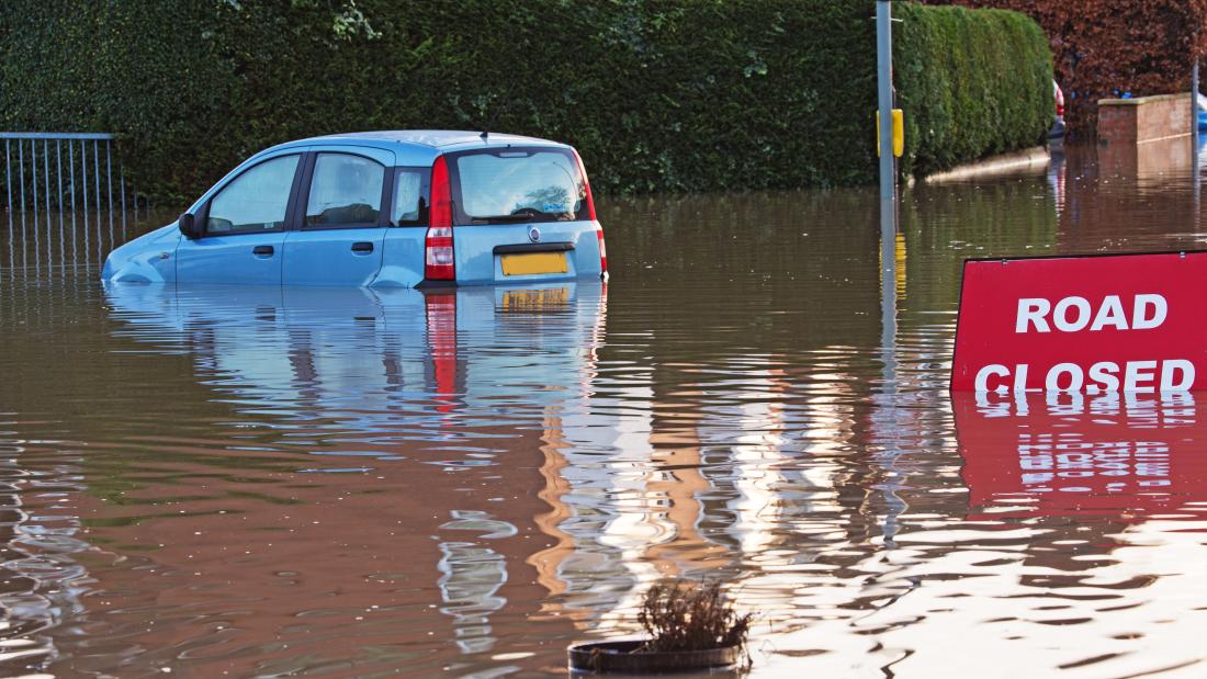  A partly submerged car in a flooded road and a sign saying Road Closed