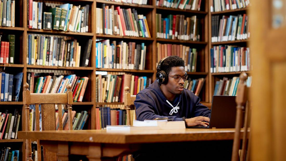 Student in Bangor University library on their laptop with headphones.