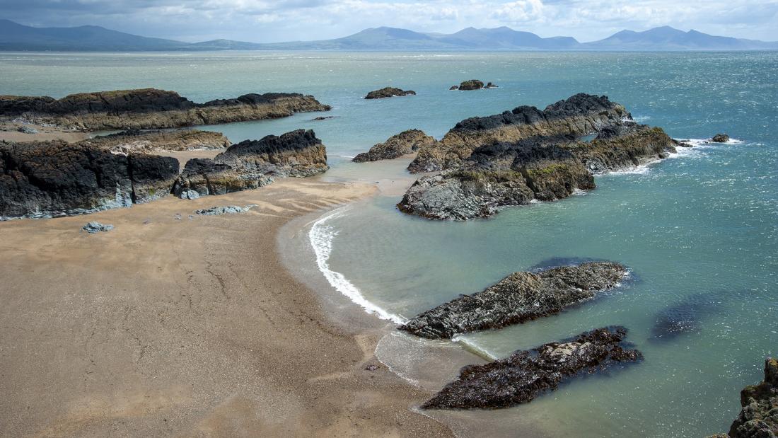 Sunny beach with rocks, blue sky and distant mountains