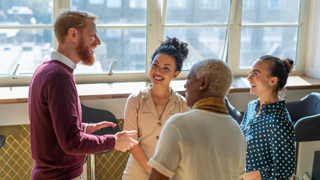 Four adults standing around having a conversation and smiling