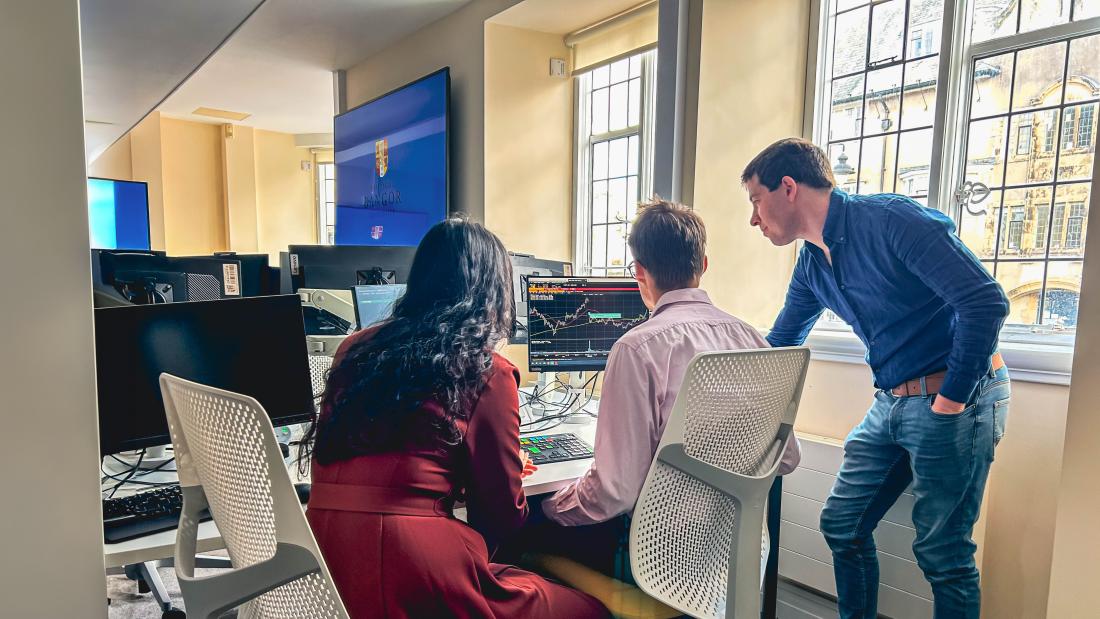 Three people sitting at a desk looking over data on a ascreen