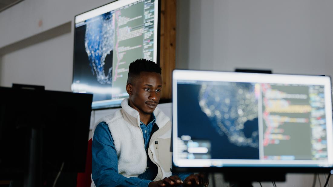A student sitting in front of a computer with a large screen in the background and a smaller screen in the foreground  
