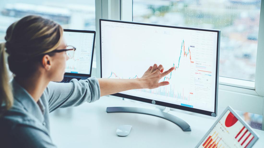 A woman points at a screen that is monitoring financial trends