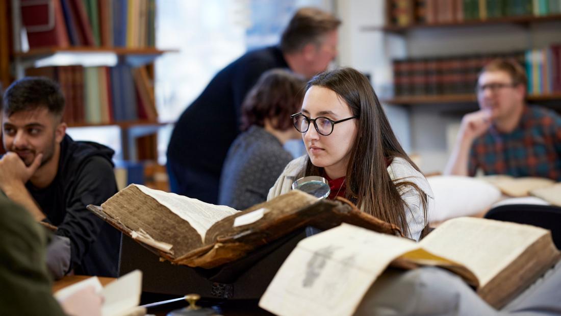 Student reading literature from large old book in a library