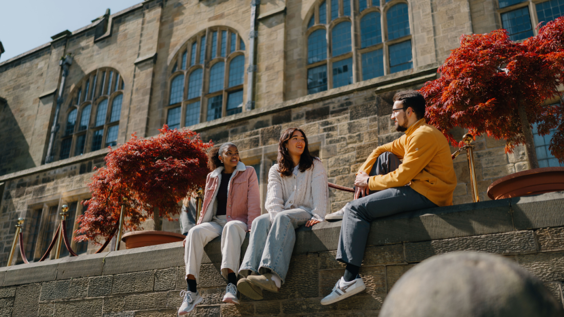Three young people chatting outside a big old building