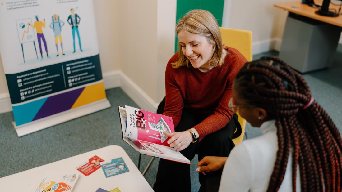 A member of staff speaking to a student and showing them a book about careers and/or employability
