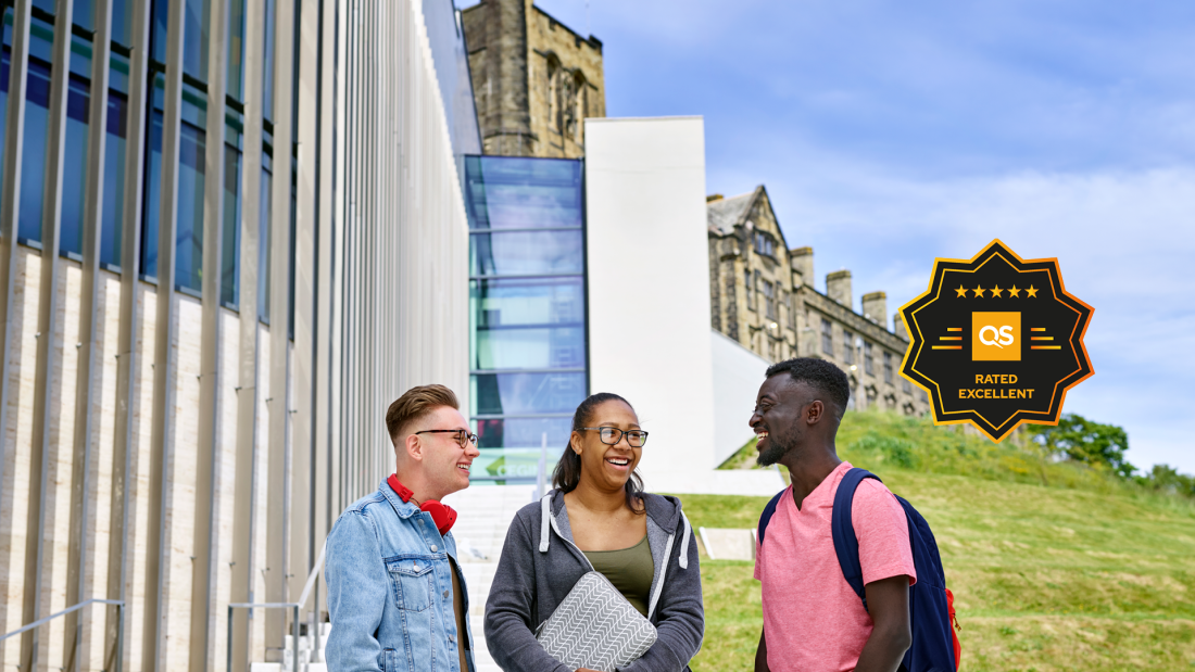 Three students standing outside Main Arts with the QS 5 star logo on the right