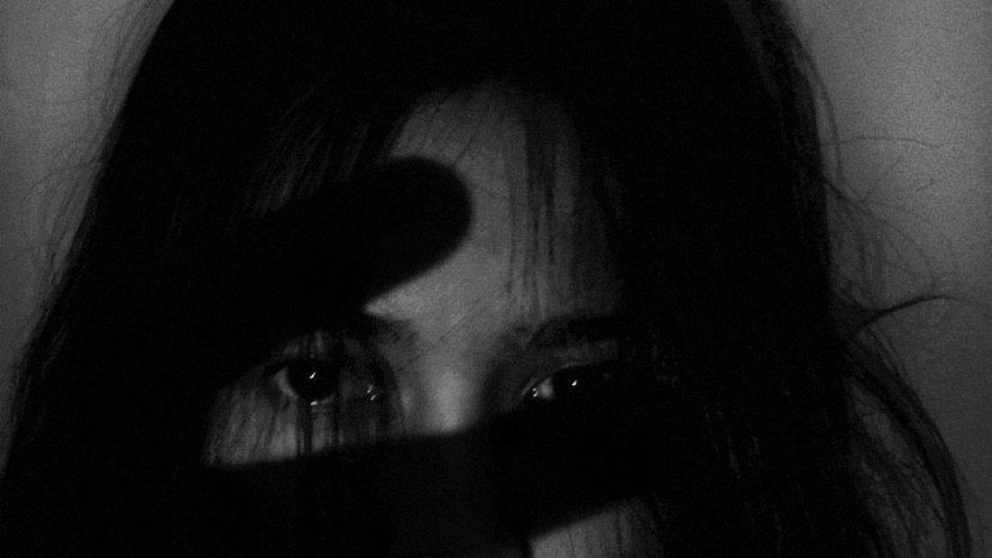 Black and white picture of a girl looking to camera with a shadow of a hand across her face