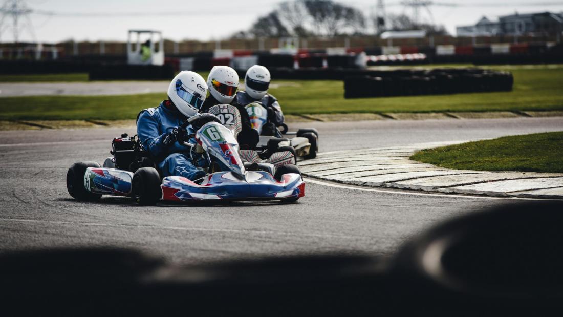 A go karting track with three individuals racing in go karts.