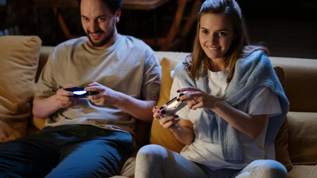 Students sitting on sofa with controllers playing a video game.