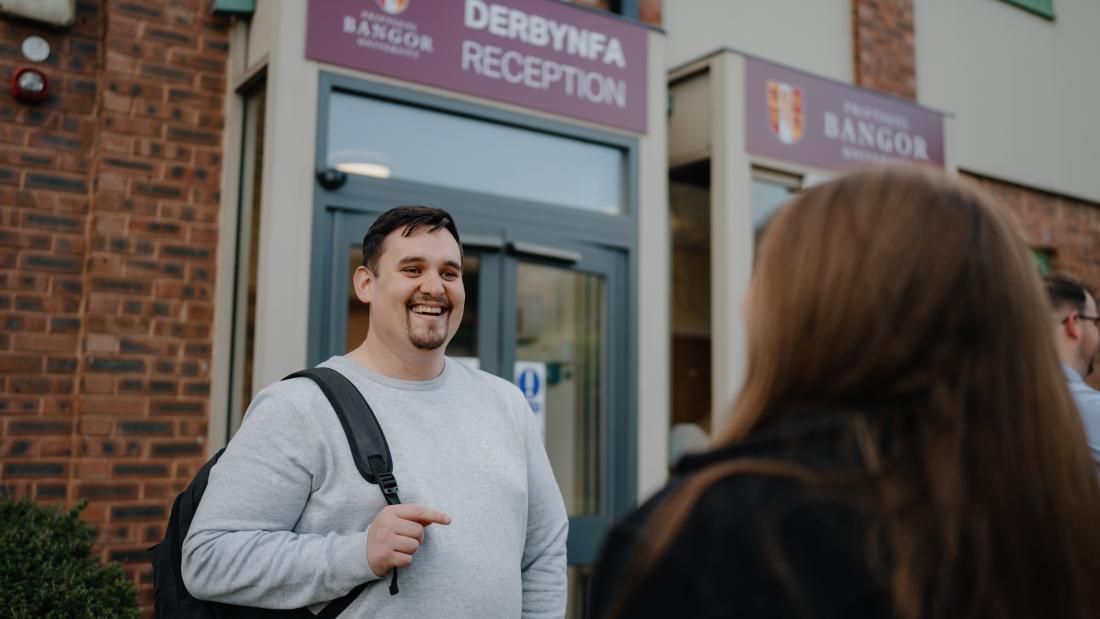 Students walking and chatting on Wrexham Campus, a Reception building is behind them