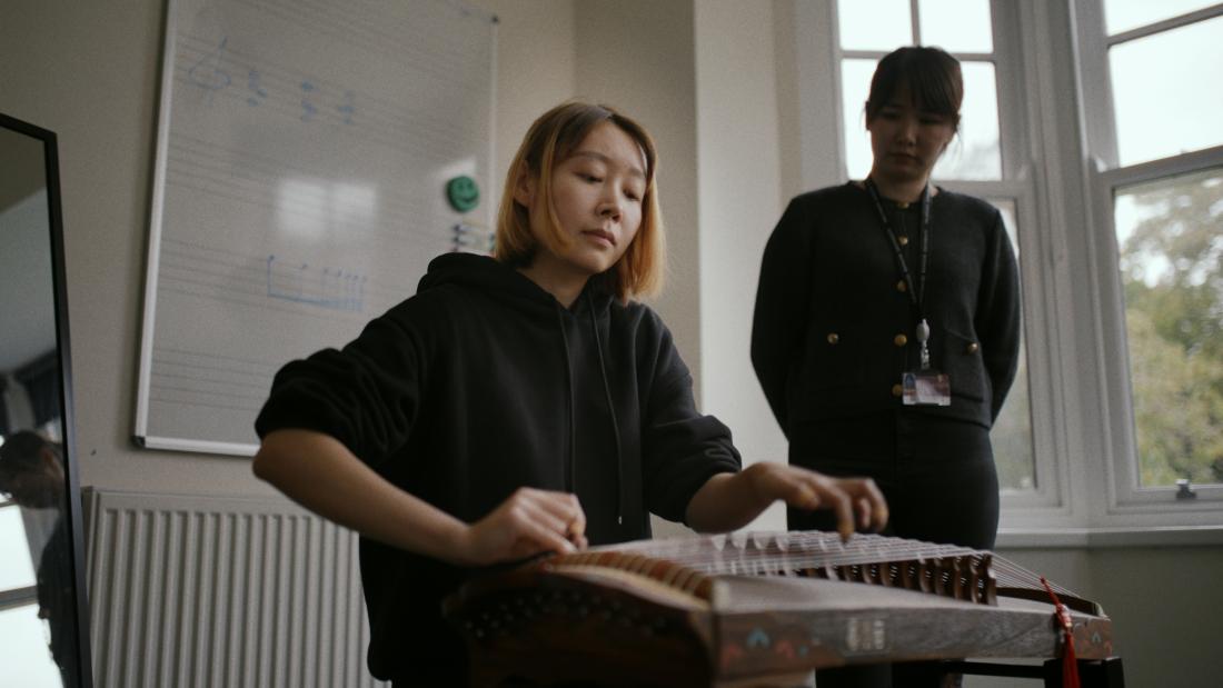 Student playing GuZheng under staff supervision