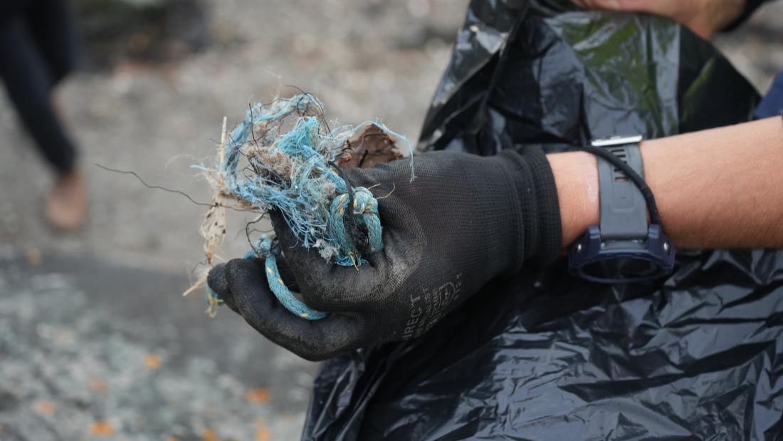 Image of a hand wearing a black rubber glove holding blue rope to put into a black bin bag