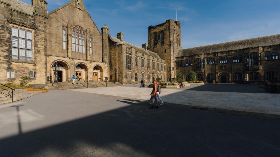 The beautifully lit Main Arts Building stands beyond the Outer Quad, as two students walk toward its entrance from the direction of the library.