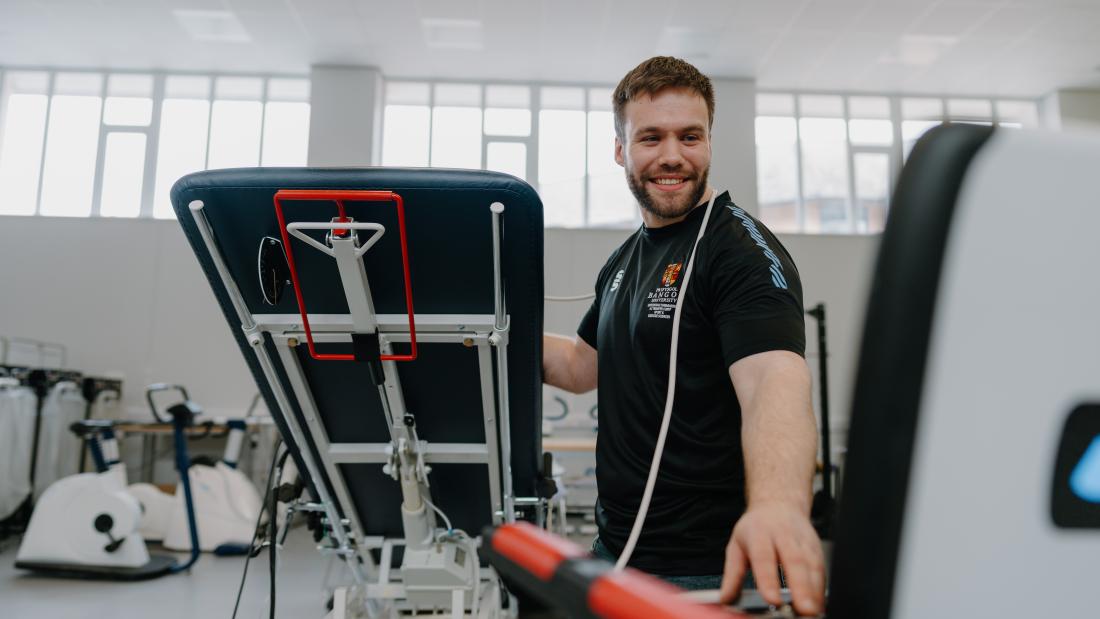 Academic in black Bangor Sport Science T-shirt doing lab work smiling at the computer