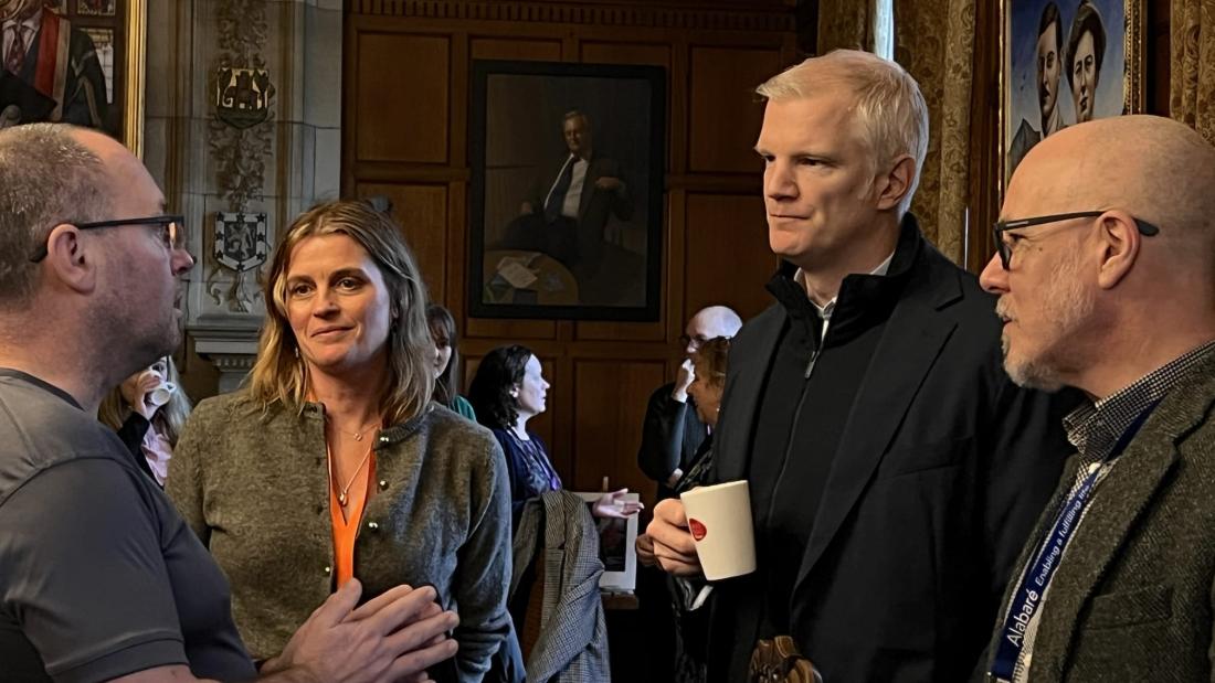 Image of three men and one woman chatting informally at an event