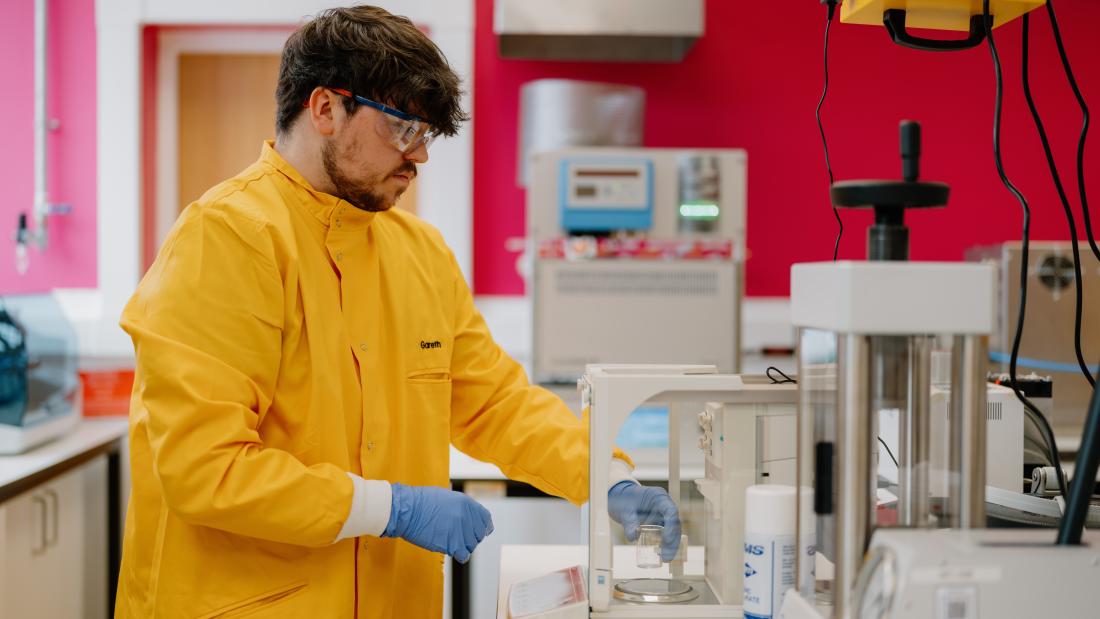 student in lab wearing a yellow lab coat conducting some sort of experiment