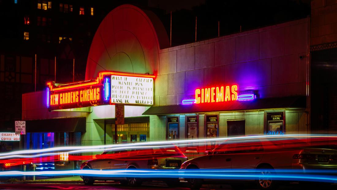 Kew Gardens Cinema in neon lights in the evening with strobe light traffic passing