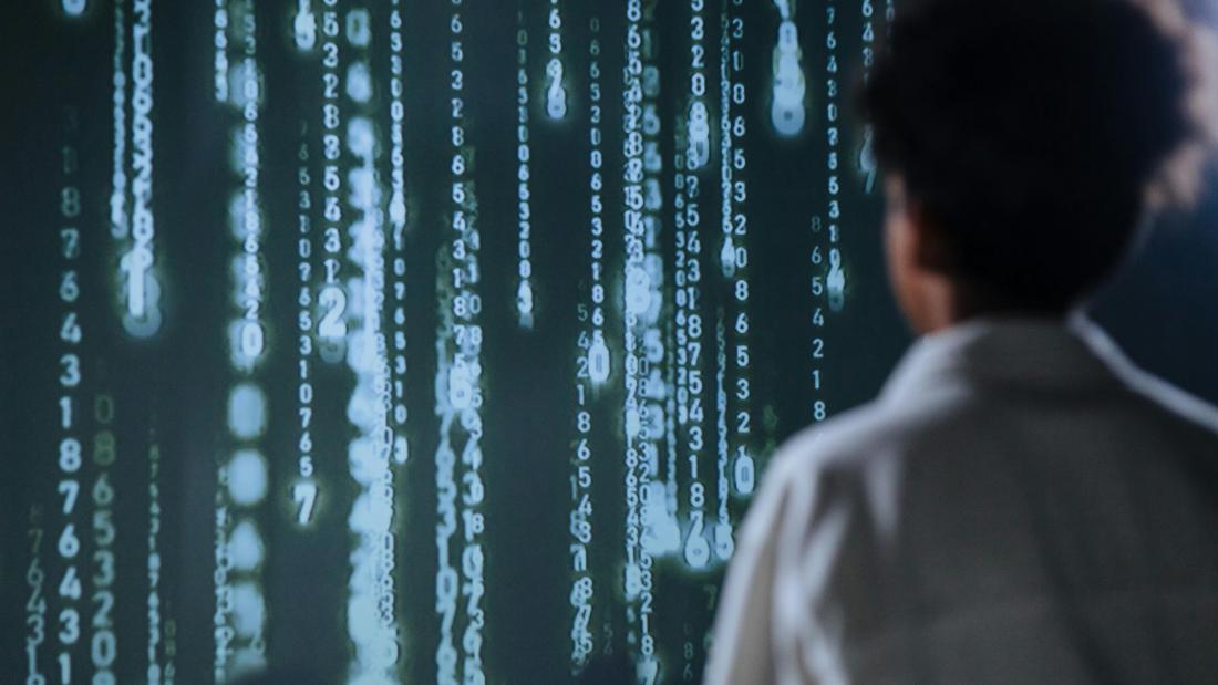 Vertial numbers falling on a black screen with an individal watching screen