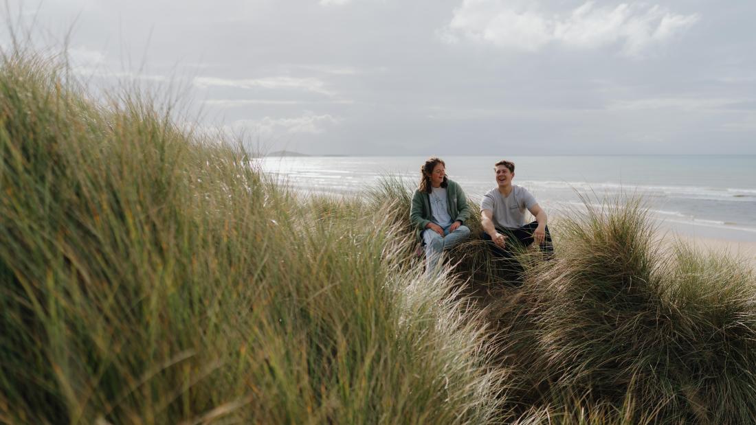 Two students sitting, chatting in the dunes