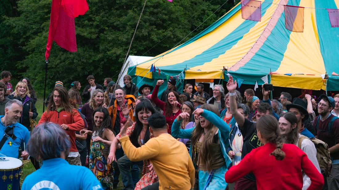 People in a field in a festival with a green and yellow marquee in the background