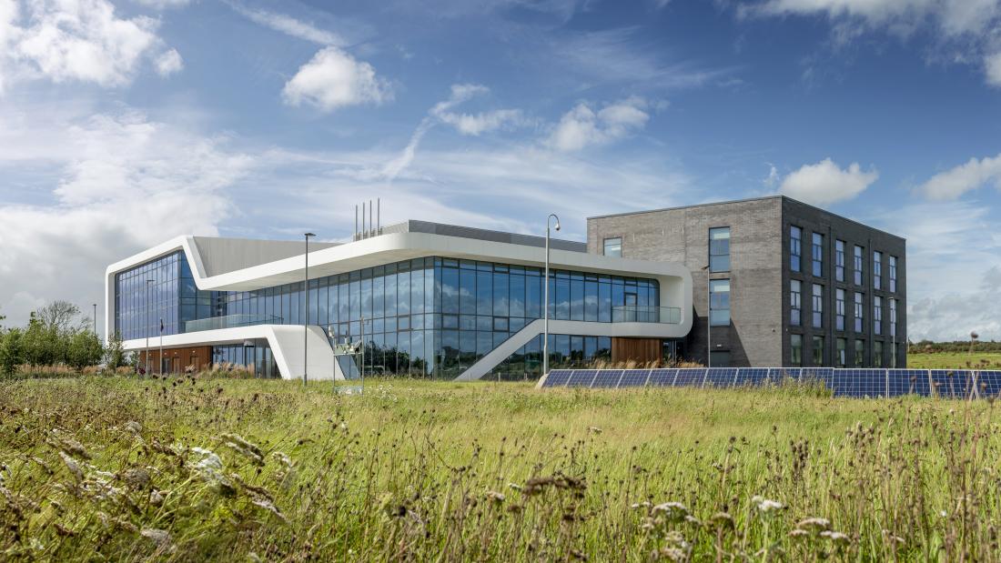 A modern building with large glass sections stands behind a grassy area with solar panels.