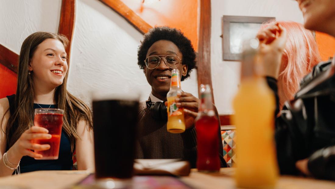 A group of students in a pub setting at a table, socialising and drinking soft drinks.