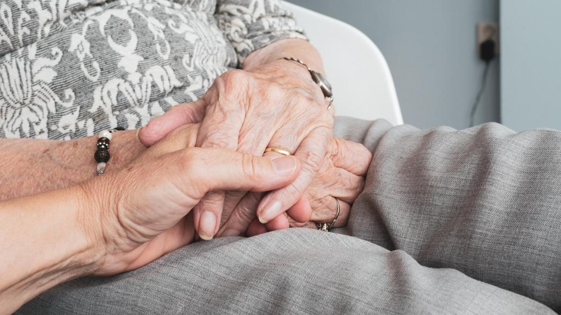 Close-up of two people holding hands, one wearing a patterned shirt and the other wearing grey pants.