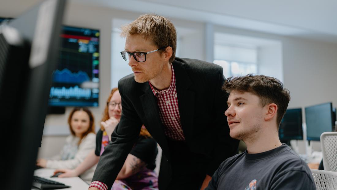 A students with a lecturer looking at the Bloomberg terminals in the University trading floor 