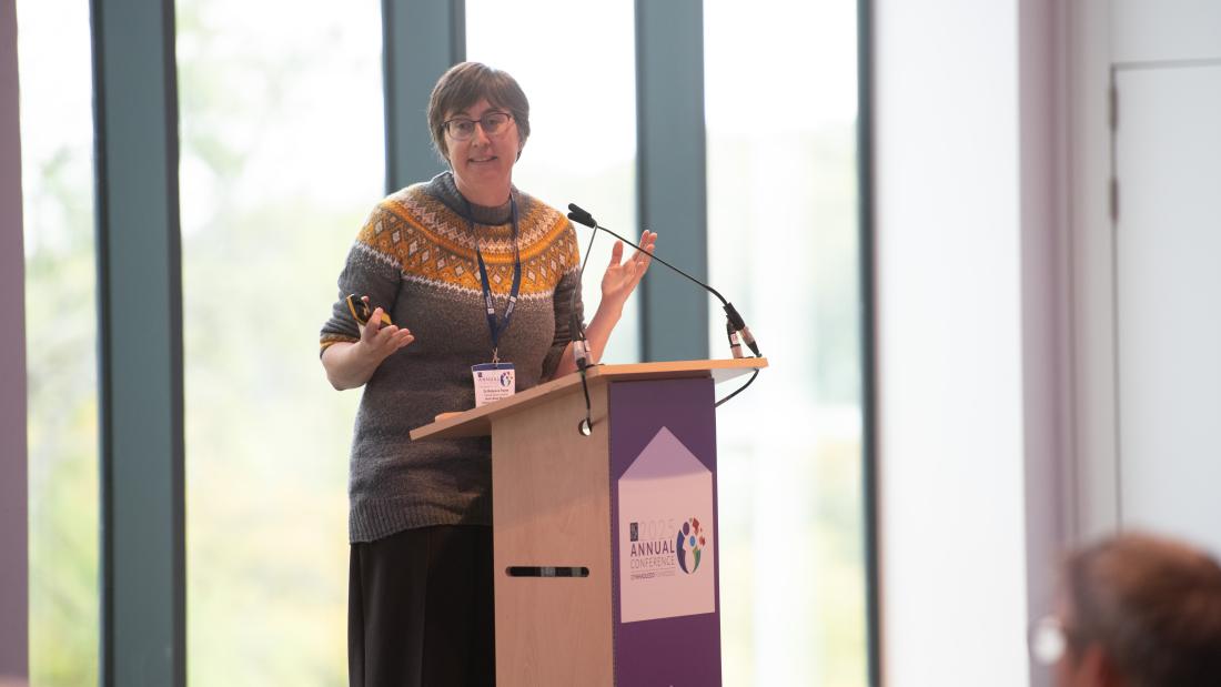 Dr Rebecca Payne, GP, Clinical Senior Lecturer at Bangor University is speaking at a lectern 