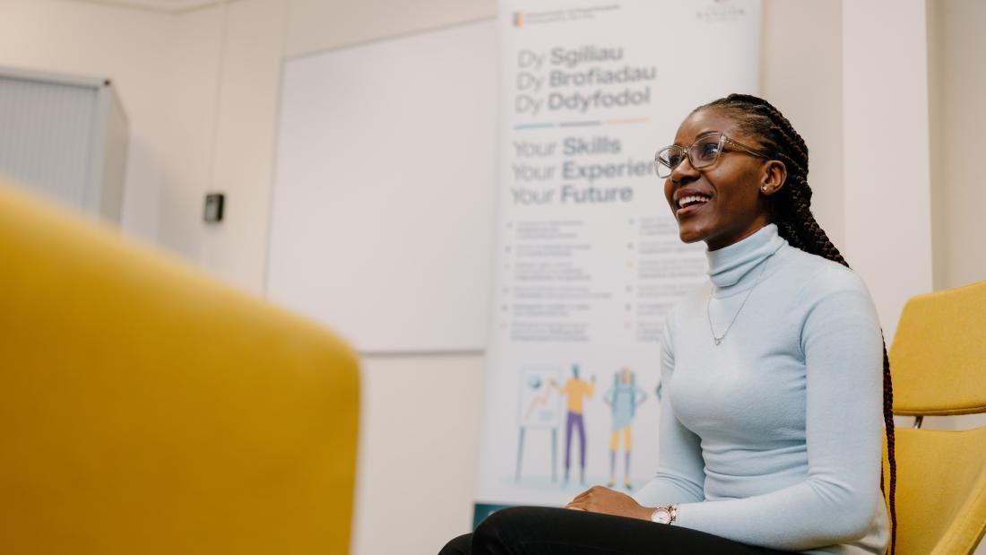 Woman sitting on a yellow chair with hands on legs looking out into the distance