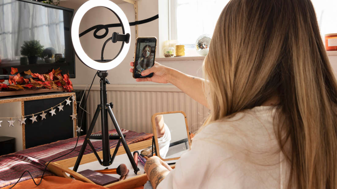 A woman holding a phone in front of a selfie ring light