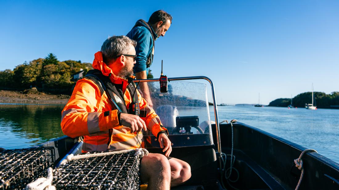 Two men on a small boat beside oyster nurseries in the Menai Strait on a sunny day