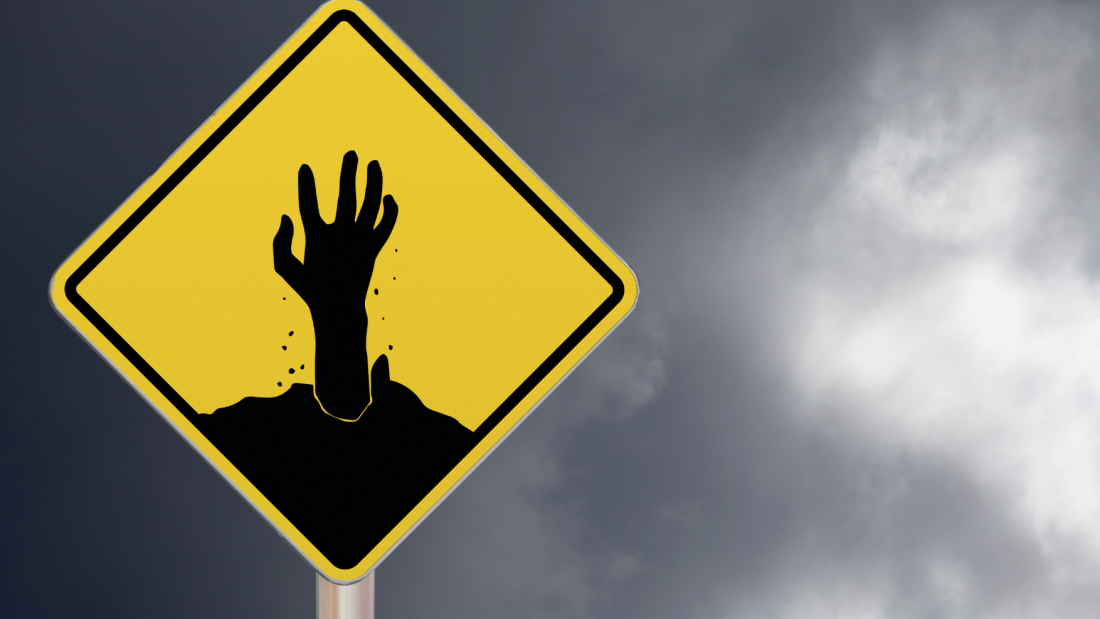 Yellow road sign with a black image of a zombie hand coming out of it.