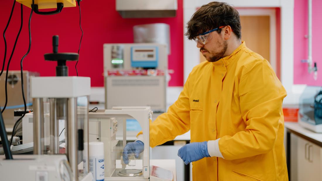 Picture of a student in a lab wearing yellow coat, blue glows and protective eyewear