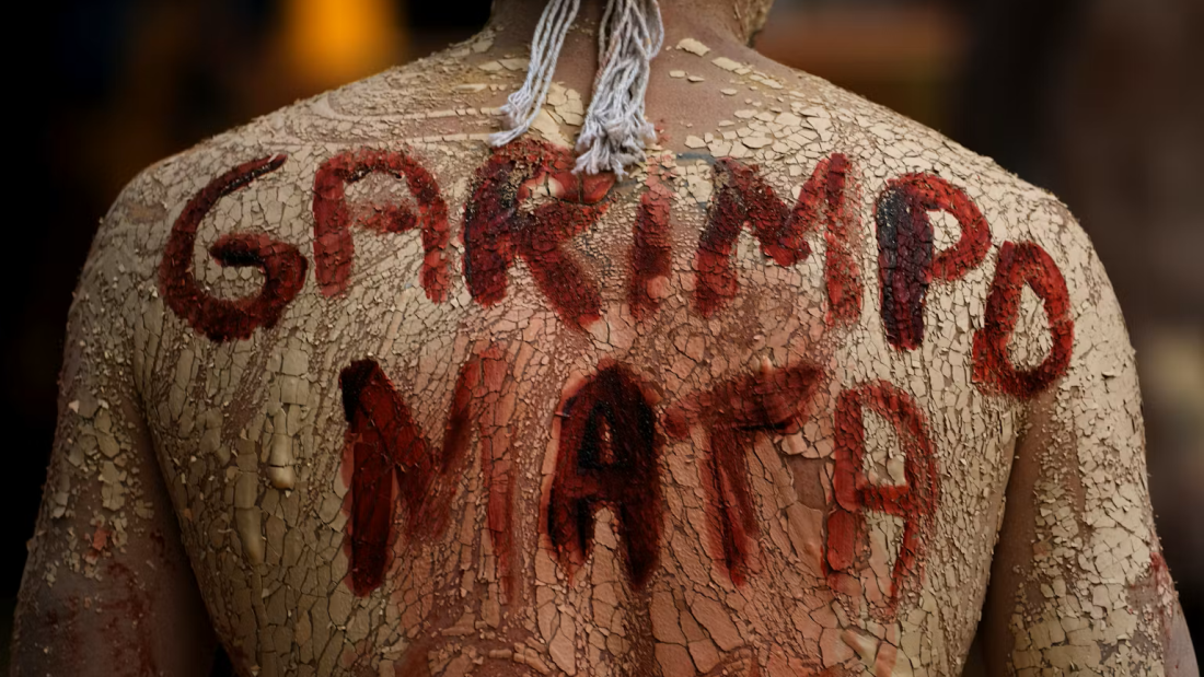 An Indigenous man with a phrase in Portuguese painted on his back 
