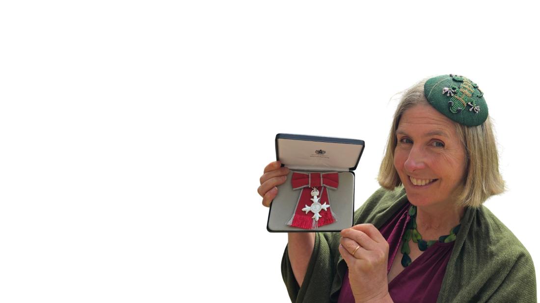 Person holding an open presentation case displaying a medal with a red ribbon, photographed against a plain white background