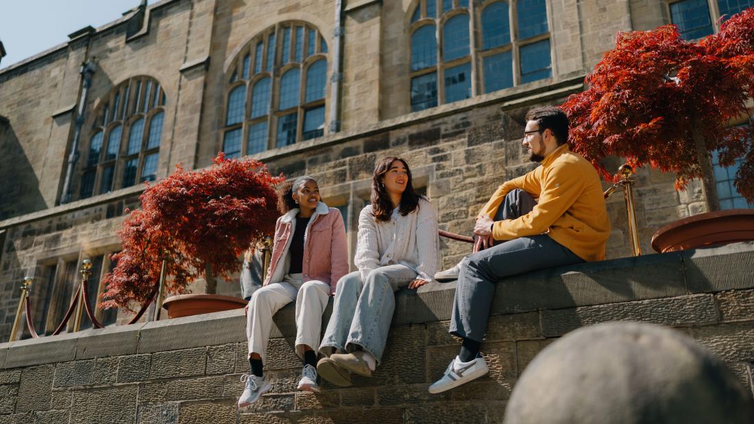 Students sitting on a wall outside a university building 