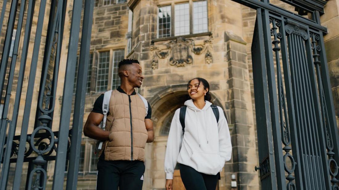 Two students chatting whilst walking through the gate in Main Arts 