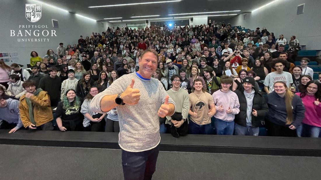 Steve Backshall with thumbs up in front of a lecture theatre full of students 