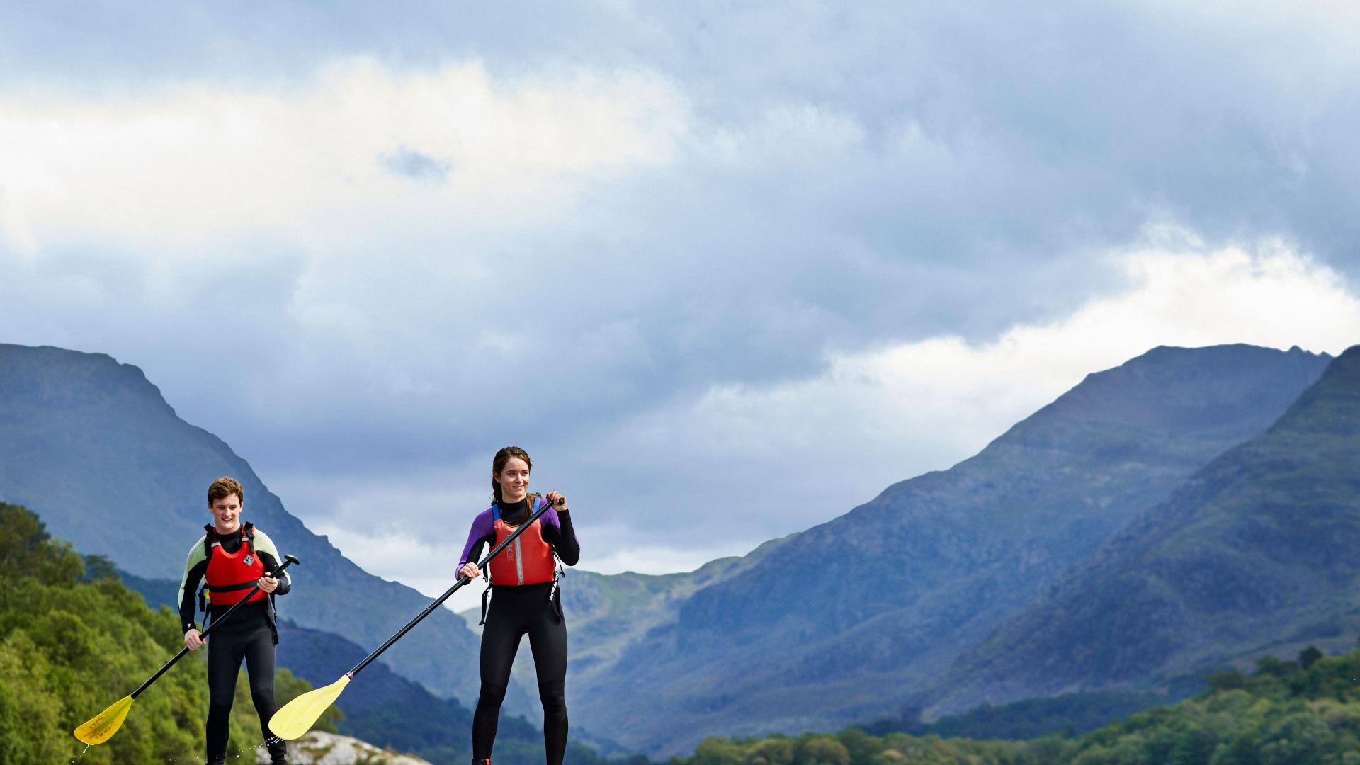 Myfyrwyr ar Fyrddau Padlo ar Lyn Padarn yn Llanberis gyda mynyddoedd Eryri yn y cefndir