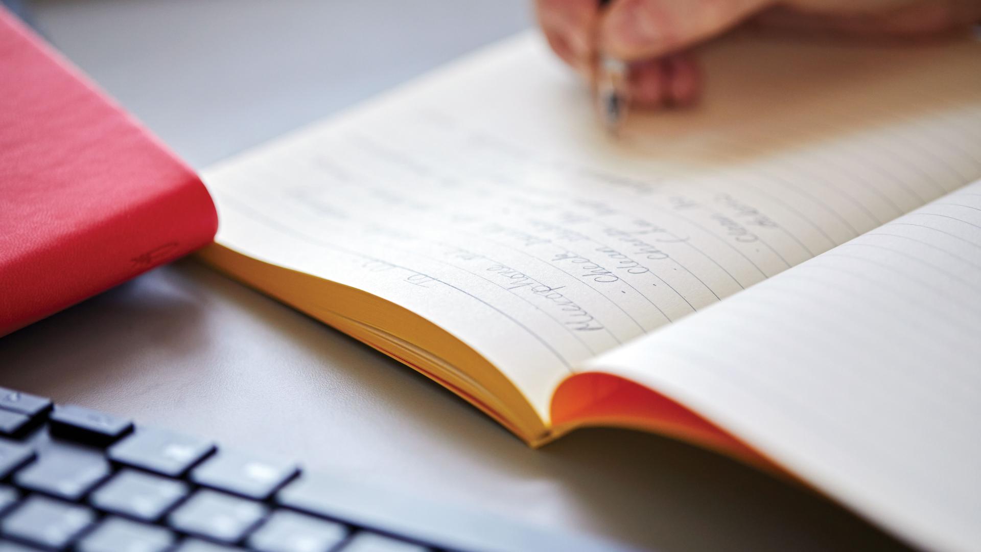 A close up of a student's hand writing notes in a notebook