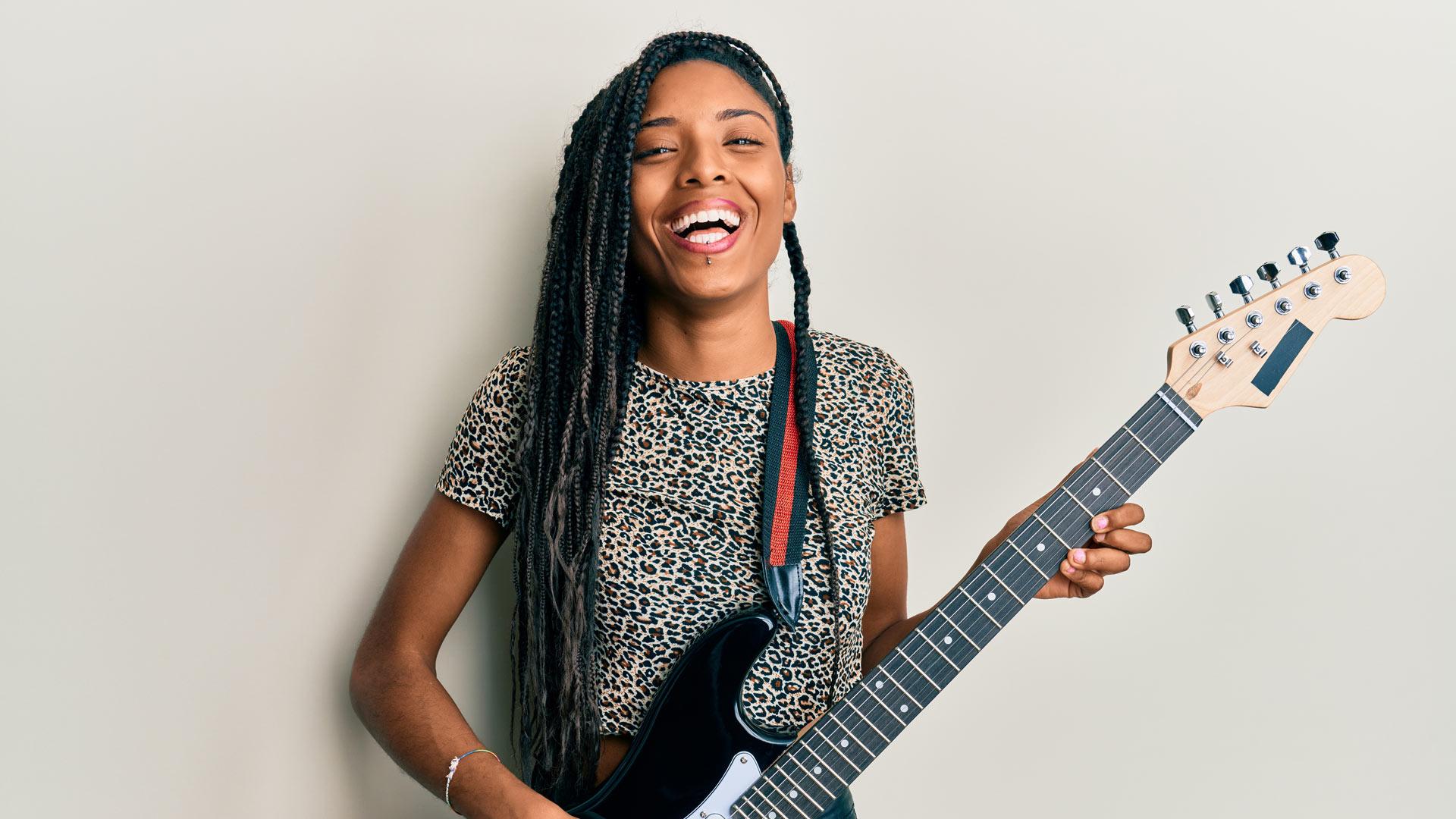 Female musician with braided hair playing guitar against a white background