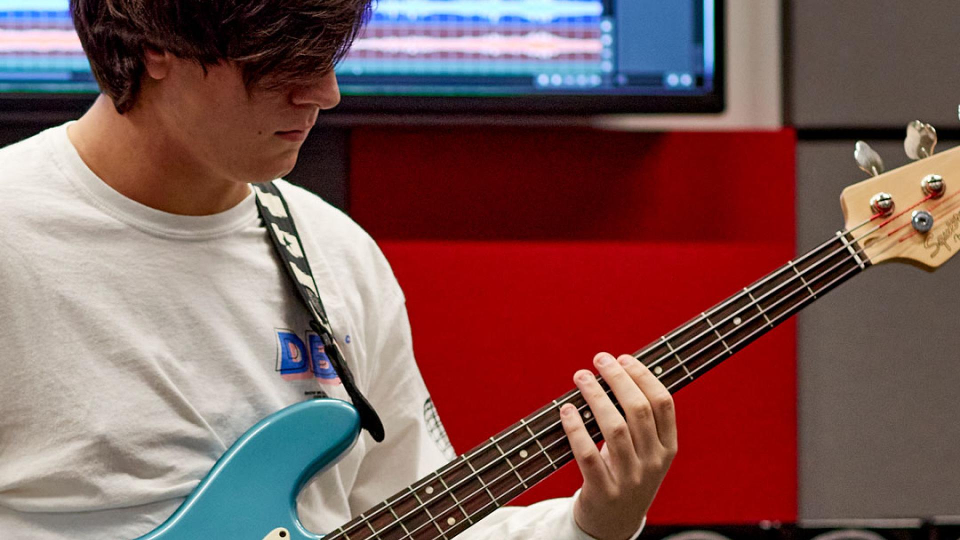 Myfyriwr yn chwarae gitar bas mewn stiwdio