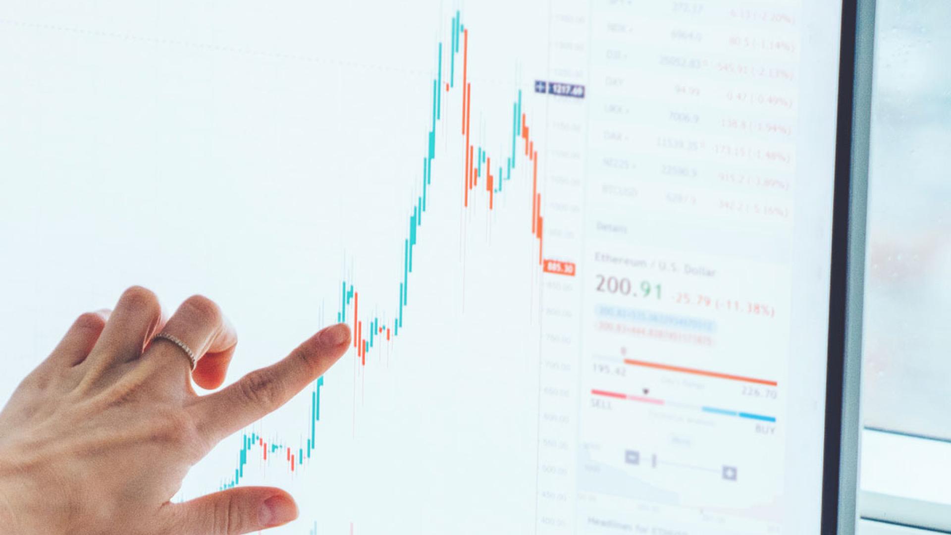 A hand pointing at a screen that is monitoring financial trends