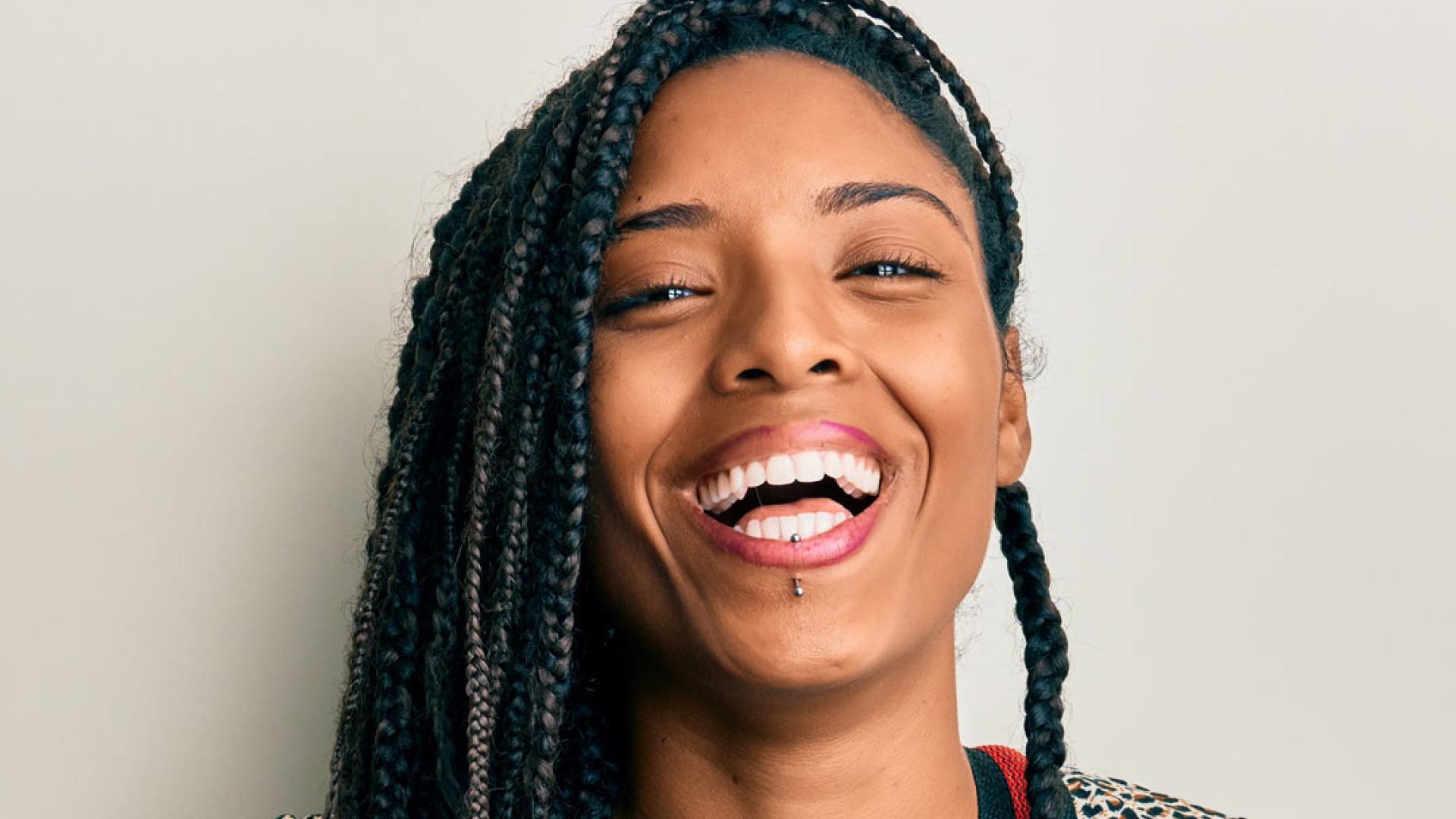 Female musician with braided hair playing guitar against a white background