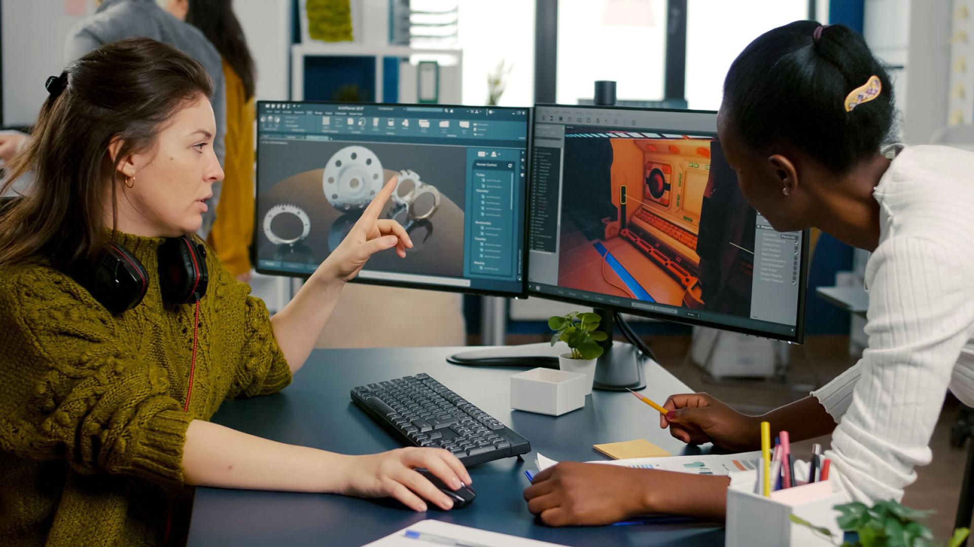 Game design student and lecturer talking around computer screen displaying code