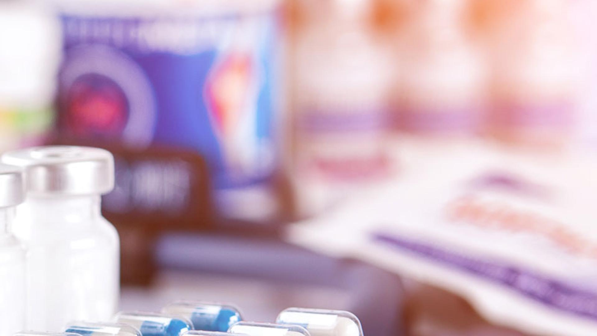 Packets of blue and yellow tablets with bottles if medicine in the background