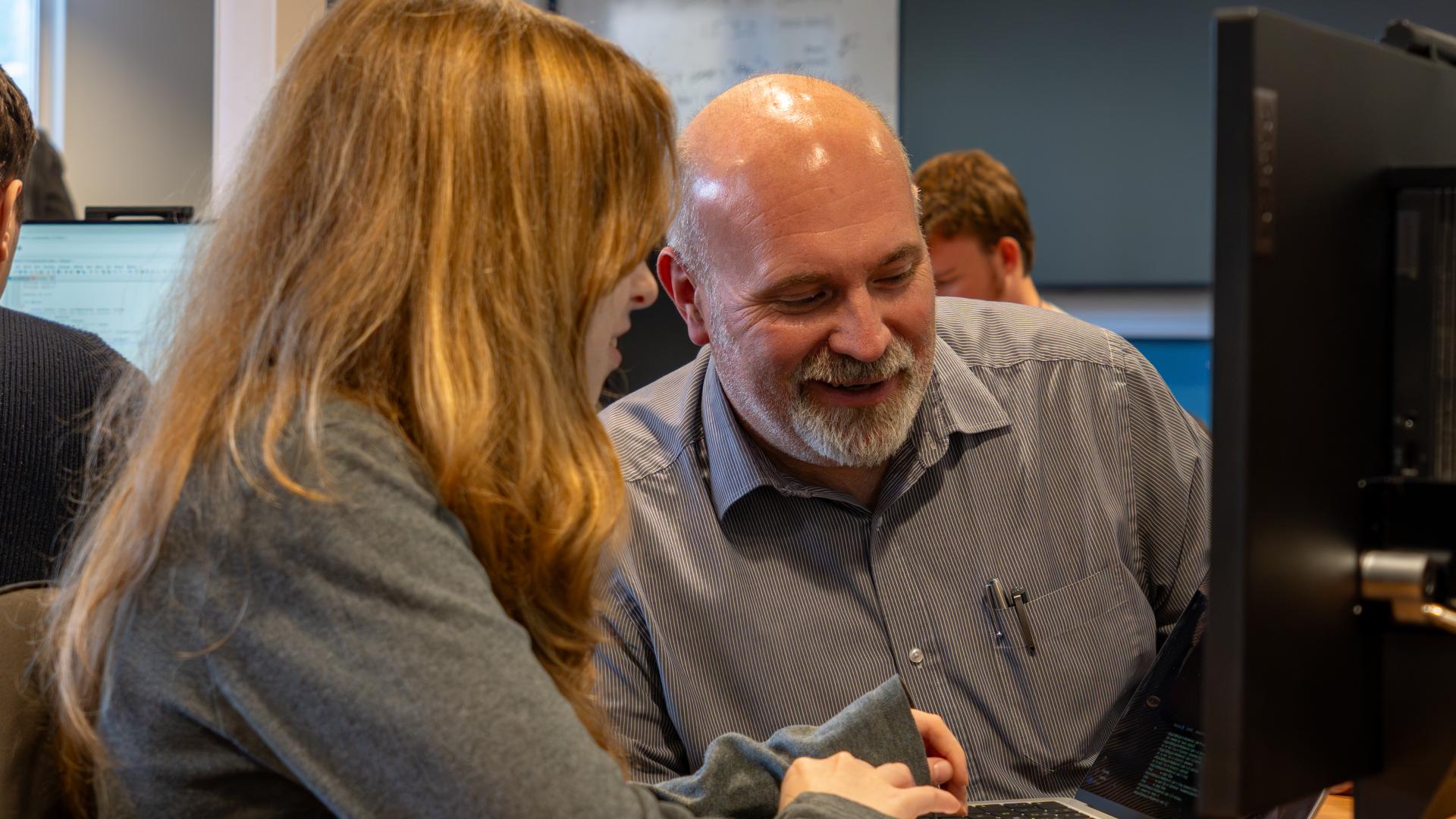 Picture of Dr Dave Perkins and a student smiling and looking at a screen of a laptop